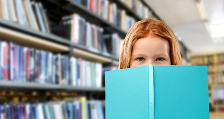 childhood and people concept - smiling red haired girl reading book over library background