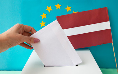 Ballot paper, hand sends a ballot box with the flag of the European Union and the flag of Latvia in...
