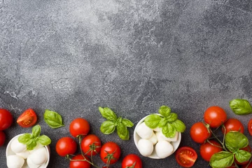 Foto op Plexiglas The ingredients for a Caprese salad. Basil, mozzarella balls and tomatoes on a dark concrete background with copy space. © Elenglush