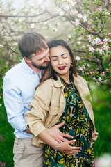 Happy and young pregnant couple hugging in nature