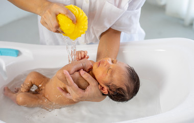 White shirt mother use yellow sponge to bath little newborn baby in white bathtub