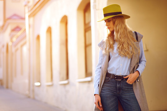 Fashionable young woman in a hat walks in the evening city. Girl in the setting sun in the city.
