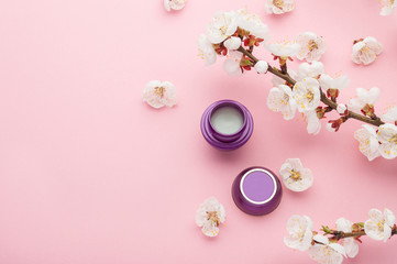 Fototapeta na wymiar Mockup for natural cosmetic skin care and spa. Jar or container with balm. Branch of blossom apricot and fallen flowers on a pink background. Natural organic cosmetics with herbal extract.