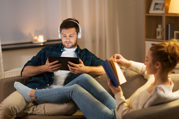 leisure and people concept - couple with tablet computer, headphones and book at home in evening