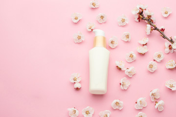 Obraz na płótnie Canvas Natural herbal lotion concept. Cosmetic product bottle with apricot blossoms on a light pink background. Blank label for branding mock-up, copy space.