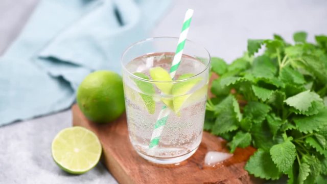 Sparkling summer cocktail with lime and mint or soda water with lime. Ice cold refreshing summer drink in glass with drinking cocktail tube