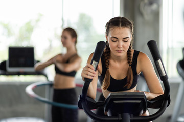 Attractive woman biking in the gym, exercising legs doing cardio workout cycling bikes. Fitness...