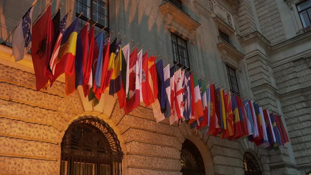 nternational flags waving on front of the beautiful architecture building in the evening time. Flags are hanging on the government building playing with light and shadow.