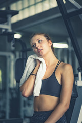 Obraz na płótnie Canvas Young attractive woman caucasian sitting and using towel to wipe the sweat. Relaxation after hard workout in gym. Fitness concept, Healthy, Sport, Lifestyle