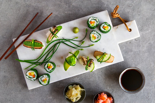 Vegan maki and nigiri sushi on white marble board over grey concrete background
