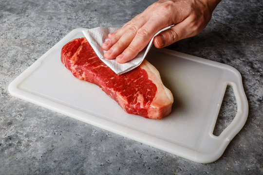 Raw fresh meat Steak Striploin on cutting board drying up excess moisture by Male hand with paper towel