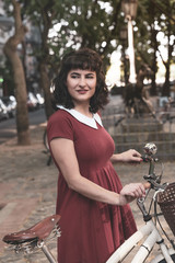 Fototapeta na wymiar A smiling woman in a red dress with a bike 
