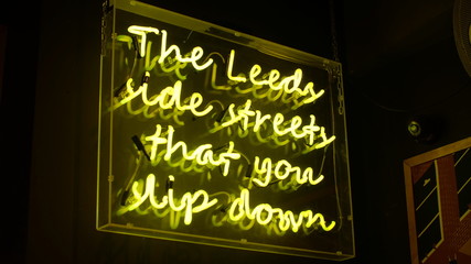 Bright fluorescent yellow neon sign that says : 'The Leeds side streets that you slip down'. The neon sign illuminates its surroundings making this a key feature to the growing establishment.