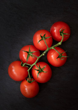 A cluster of tomatoes on vine against a black background.