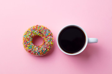 Coffee with donut on pink paper background. Top view. Copy space.