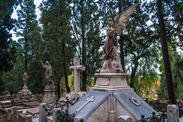 Obraz premium Several graves with sculptures on the background of trees on the Montjuic Cemetery in overcast day, Barcelona, Catalonia, Spain