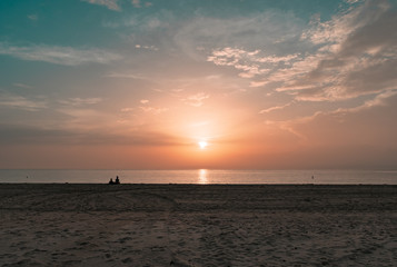 silhouette of a couple sitting on the sand watching the sun rise on a calm morning