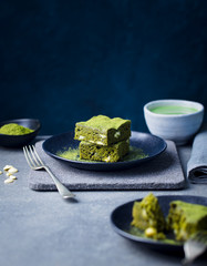 Matcha green tea cake, bars, brownie with white chocolate on a plate. Grey stone background. Copy...
