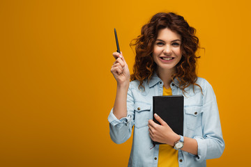 happy redhead young woman holding notebook and pen on orange