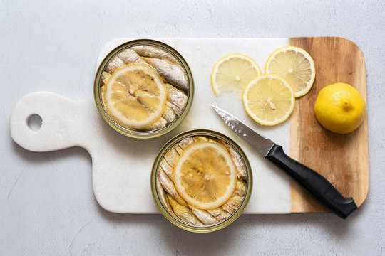 Two cans of sardines in oil with slices of fresh lemon.