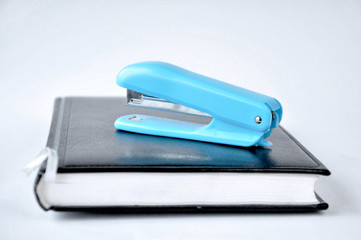 blue stapler stands on black notepad on white background