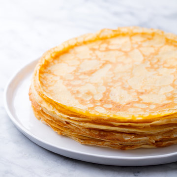 Crepes, thin pancakes, blini on a white plate. Marble background. Close up.