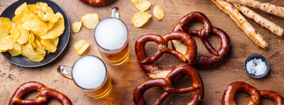 Beer, salted pretzels, potato chips, cheese sticks on wooden background. Top view.