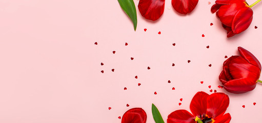 Red tulips and heart shaped confetti on pastel pink background top view Flat lay copy space. Mother's Day, Valentines Day, birthday, holiday background. Spring flowers, Lovely greeting card