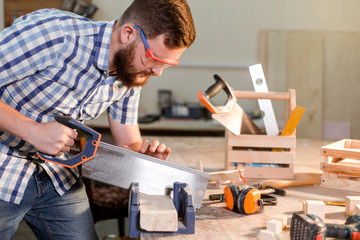 Working days of a professional carpenter in a home workshop, a craftsman at his workplace sawing...