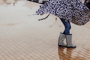 Stylish woman in a raincoat and rubber boots walks through the puddles and have fun