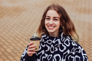 Stylish woman in raincoat walking through urban area, holding takeaway coffee in hand