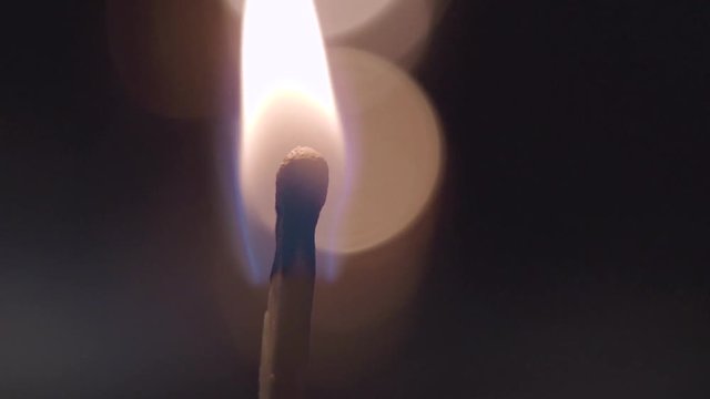 Close-up of burning match in male hands on a dark background.