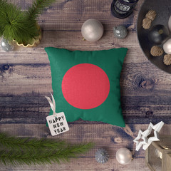Happy New Year tag with Bangladesh flag on pillow. Christmas decoration concept on wooden table with lovely objects. © sezerozger