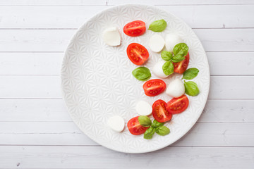Caprese salad of tomatoes, mozzarella cheese and Basil on a white plate. Italian cuisine. Copy space