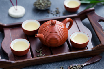 Green tea in tea pot and bowls, cups on wooden tray. Close up.