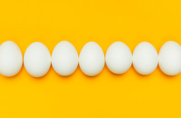 Creative food minimalistic background, Easter. White chicken eggs on yellow background top view...