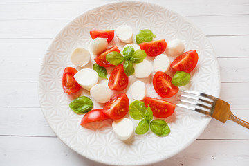 Caprese salad of tomatoes, mozzarella cheese and Basil on a white plate. Italian cuisine.