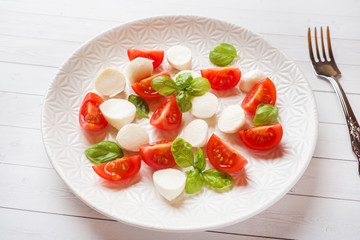 Caprese salad of tomatoes, mozzarella cheese and Basil on a white plate. Italian cuisine.