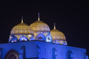 Al Ameen City Mosque glowing at night purple and yellow in Muscat, Oman.