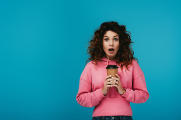 surprised young woman holding paper cup with drink on blue