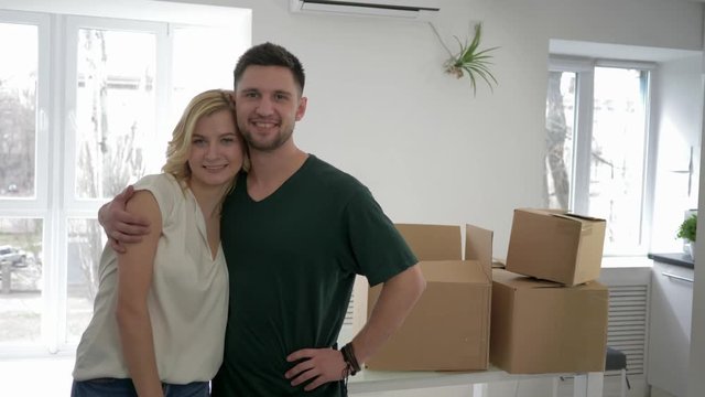 relocation at rented home, portrait of newlyweds new apartment owners show keys to flat and hug while housewarming on background of cardboard boxes