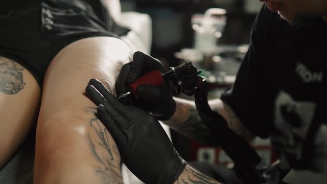 professional tattoo artist introduces ink into the skin using a needles from a tattoo machine. color tattoo art on body. Makes a tattoo. Professional tattooist working tattooing in studio