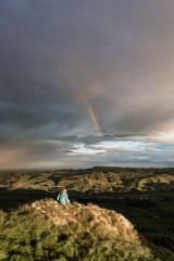 Girl under a rainbow looking out over rolling hills from Te Mata Peak