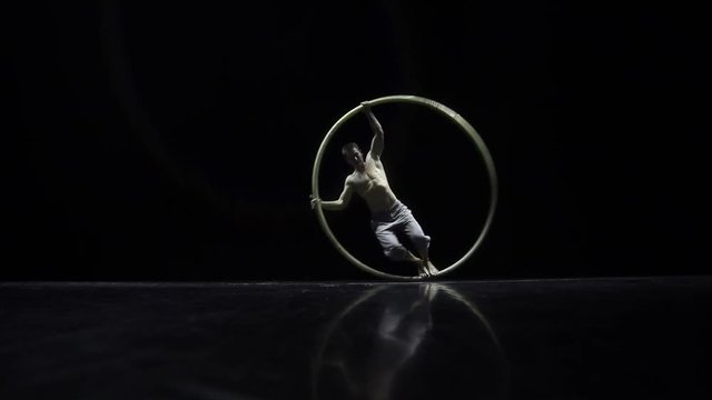 Circus performer artist in a Cyr Wheel in theatre on a black background