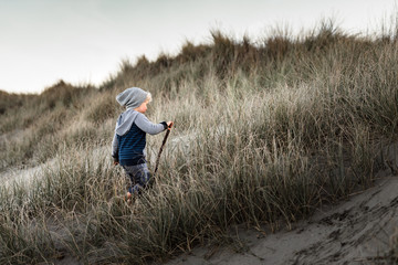 Boy with stick hiking up sand dune