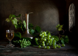 Green grapes and white wine with metal jug. Still life in vintage style in dark key