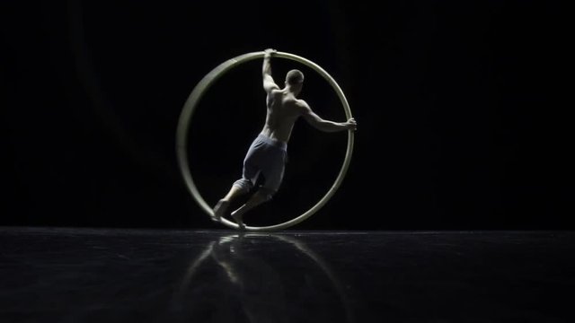 Muscular circus artist in the Cyr Wheel doing difficult tricks slow motion