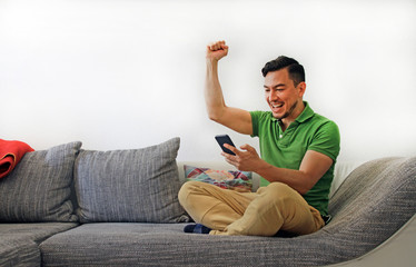 Man on couch excited by news on smartphone