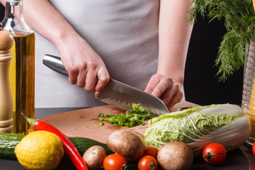 young woman slicing herbs in a gray apron