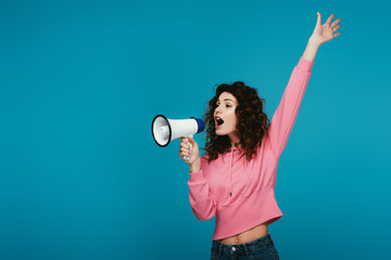 attractive curly redhead girl screaming in megaphone on blue